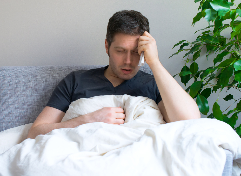 A man sitting in bed having headaches due to prescription drug abuse withdrawal 